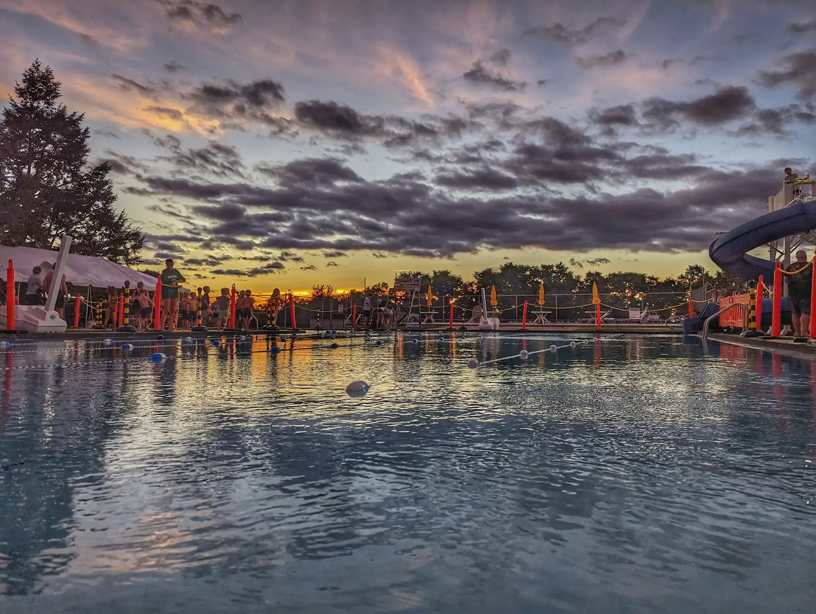 The Main Pool at dusk under heavy clouds, with umbrellas and the slide on the far deck